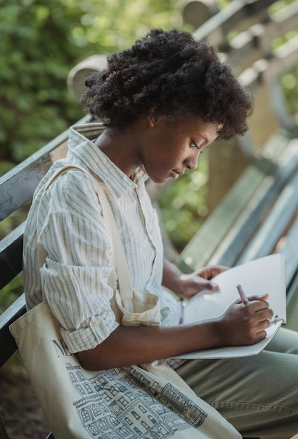 Teenage Girl Sitting on the Bench in the Park and Making Notes