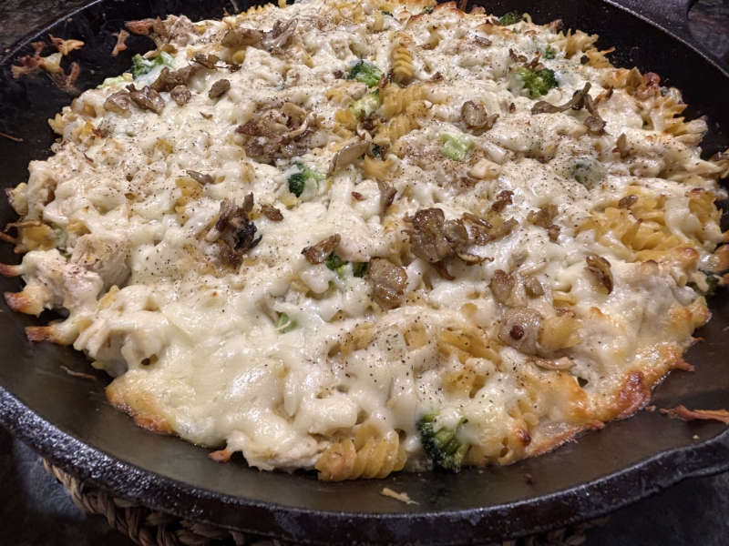 picture of One Skillet Chicken Tetrazzini Bake with melting cheese and sautéed mushrooms on top in a black cast iron skillet