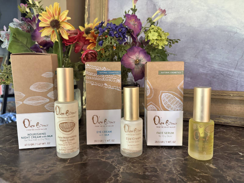 A wide shot of Olea Essence Night Cream, Eye Cream, and Face Serum with their boxes and spring flowers.