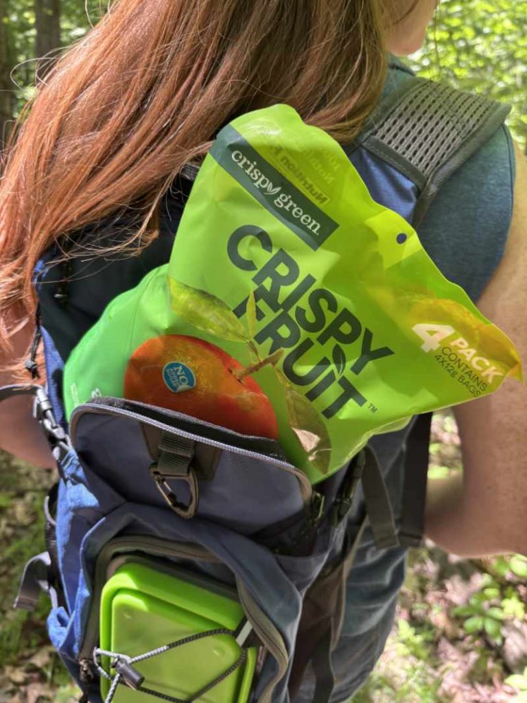 picture of red headed woman with blue backback hiking with Crispy Green Crispy Fruit Freeze Dried Fruit Review portable healthy snack in backpack