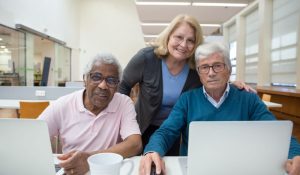 two older men at laptop computers with woman standing behind education