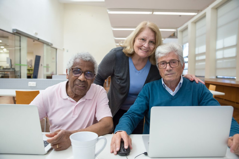 two older men at laptop computers with woman standing behind education